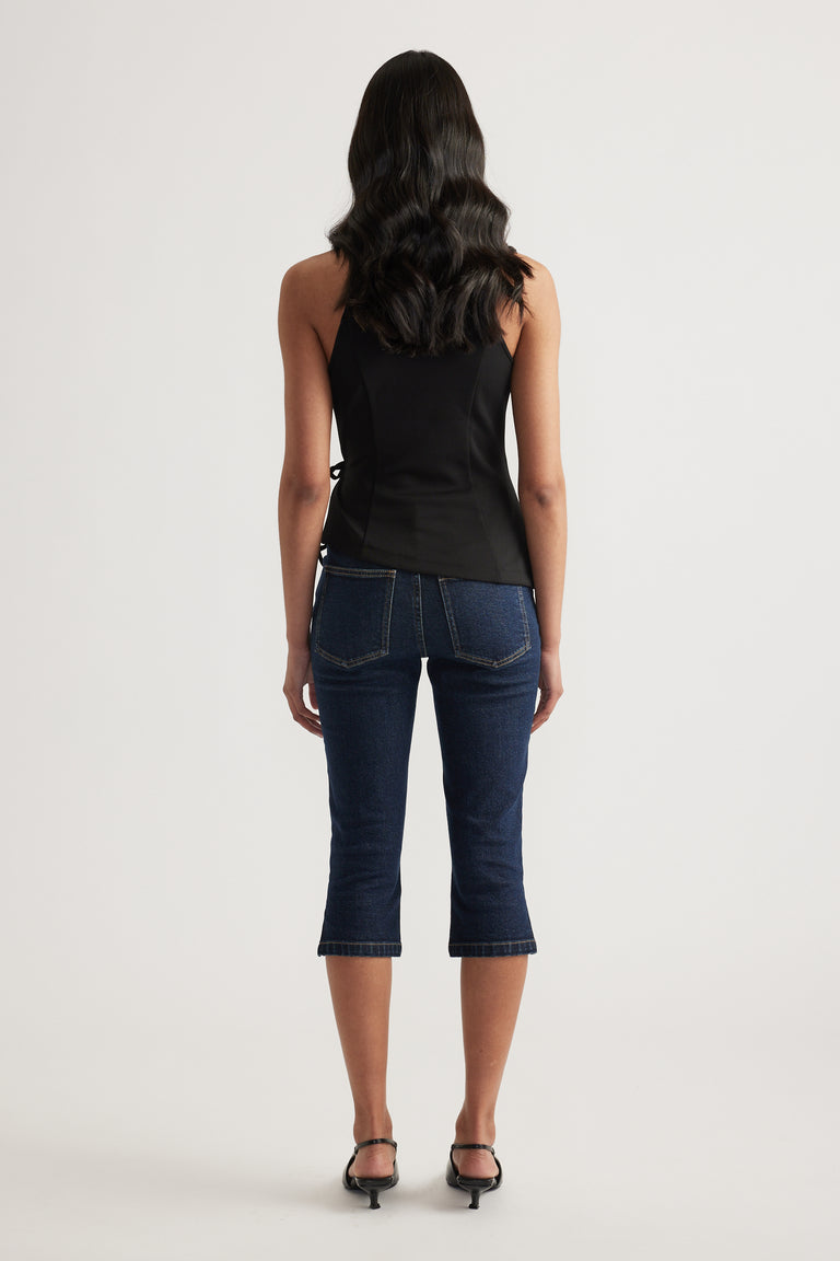 Back view of woman wearing a black sleeveless wrap halter top with dark cropped jeans and black heels