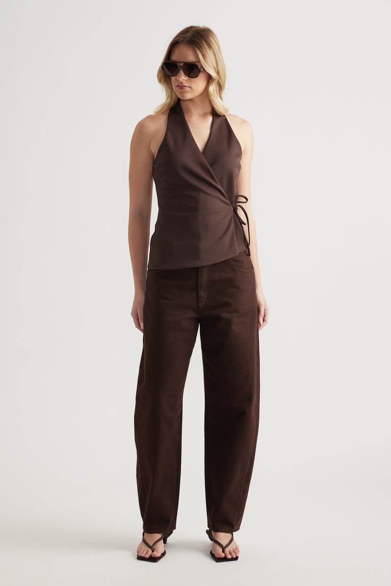 Woman wearing a brown sleeveless wrap top with a side tie, wide leg pants, sunglasses and flat sandals