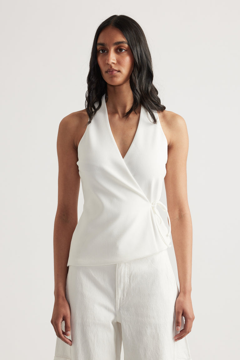 Woman wearing a white sleeveless wrap halter top with a V neck and side waist tie with matching pants