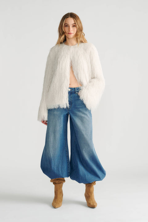 Woman wearing an ivory fringed jacket paired with loose, wide-leg denim jeans and tan slouchy boots.