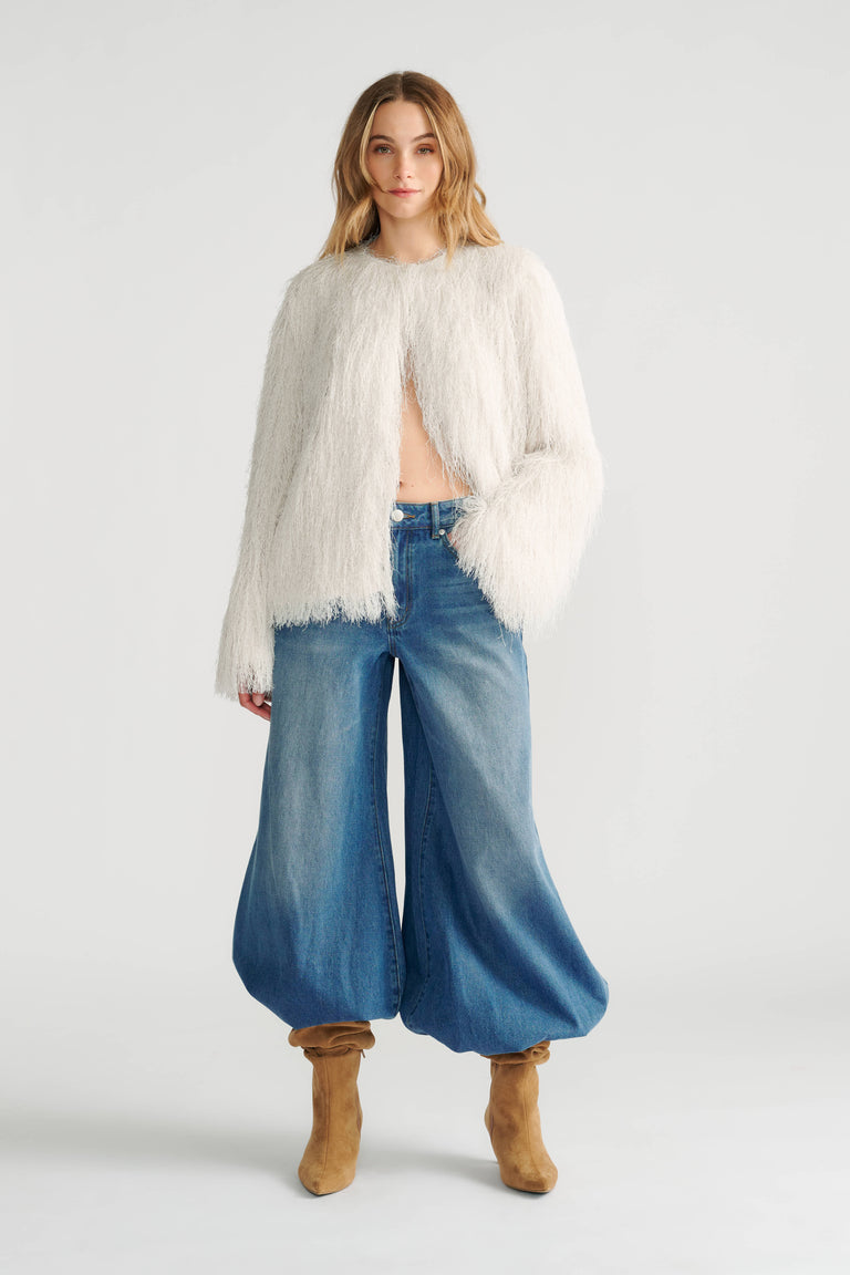 Woman wearing an ivory fringed jacket paired with loose, wide-leg denim jeans and tan slouchy boots.