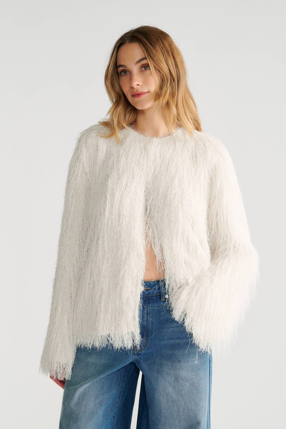 Woman wearing an ivory fringed jacket with a soft texture paired with relaxed blue denim jeans for a casual look.