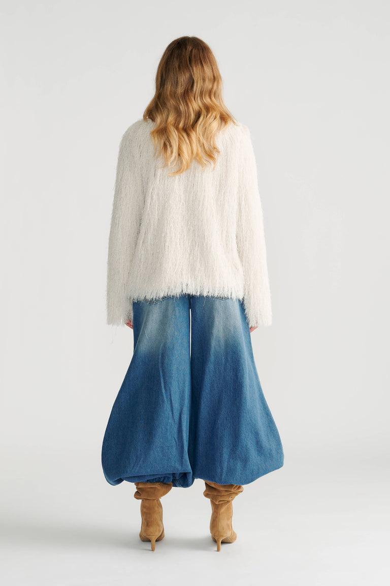 Back view of woman wearing a soft ivory textured jacket paired with wide-leg faded denim pants and tan ankle boots.