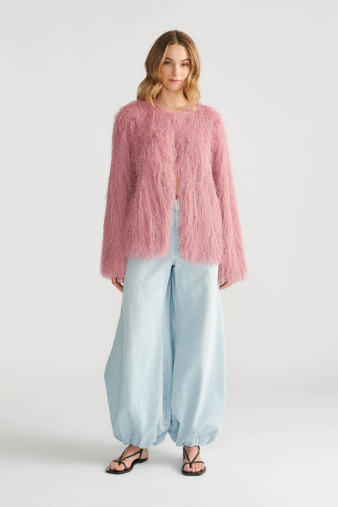 Woman wearing a soft pink fringed jacket paired with wide-leg light blue denim pants and black sandals.