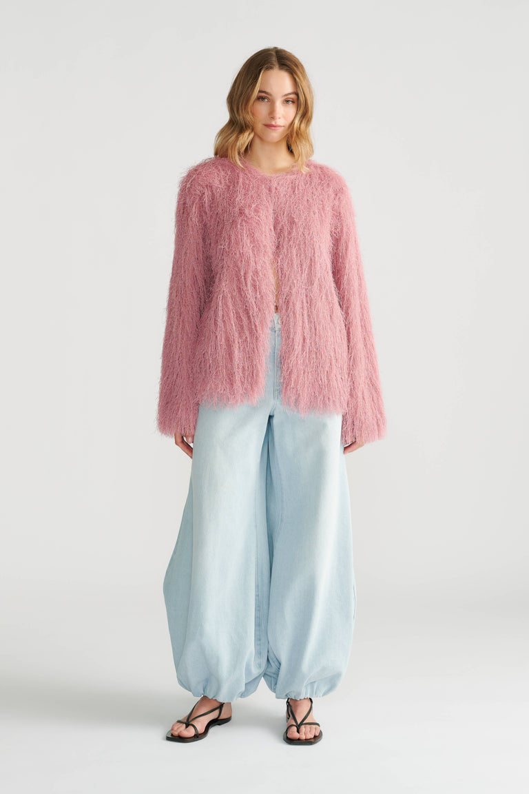 Woman wearing a soft pink fringed jacket paired with wide-leg light blue denim pants and black sandals.