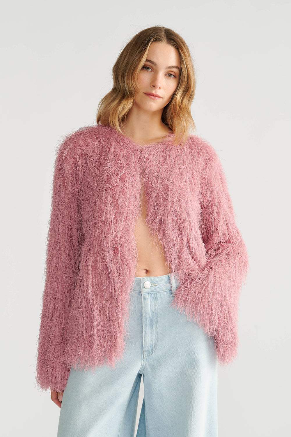 Woman wearing a soft pink fringed jacket paired with light blue high-waisted wide-leg jeans in a relaxed style.