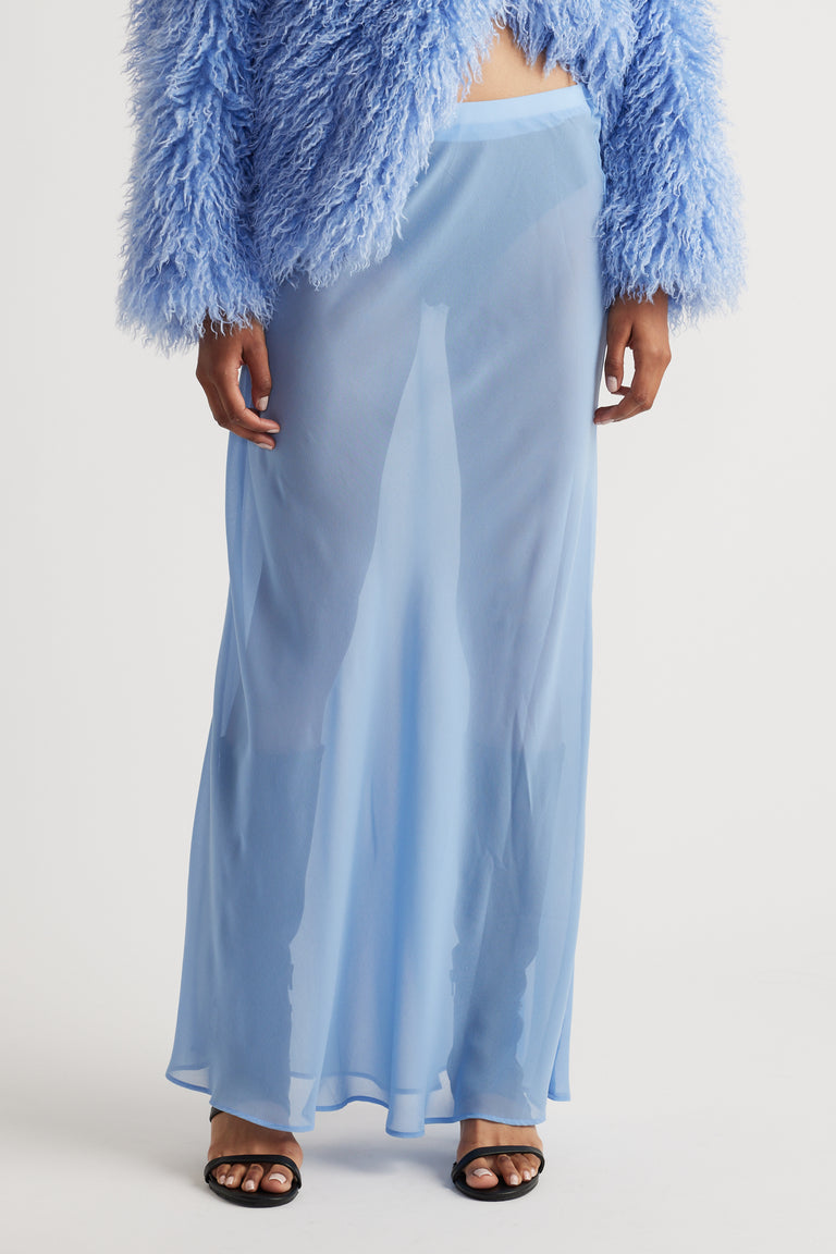 Sheer light blue maxi skirt with a flowy silhouette paired with a textured, fluffy cropped jacket and black sandals.