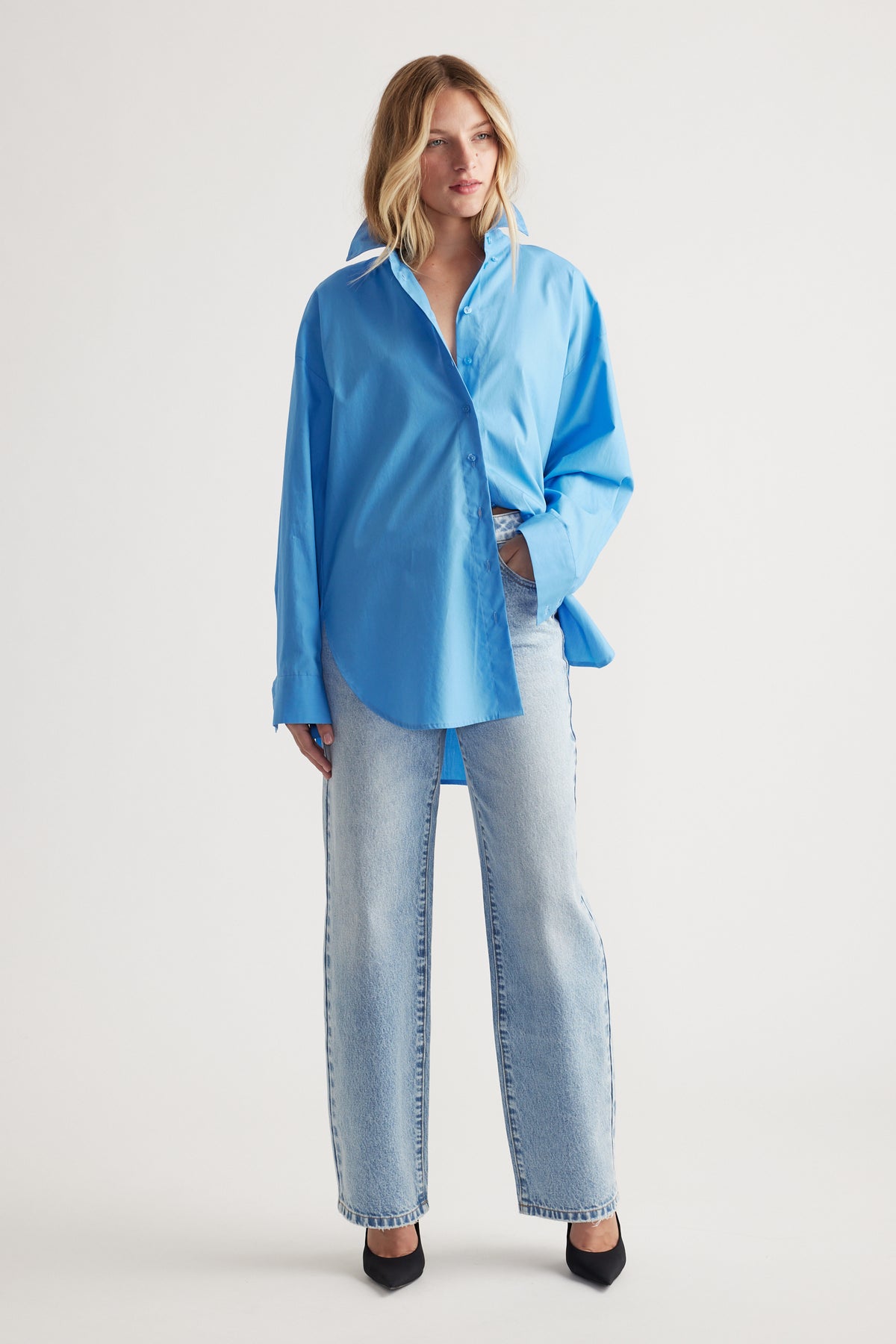 Woman wearing a relaxed fit bright blue oversized shirt paired with light wash straight-leg jeans and black heels.