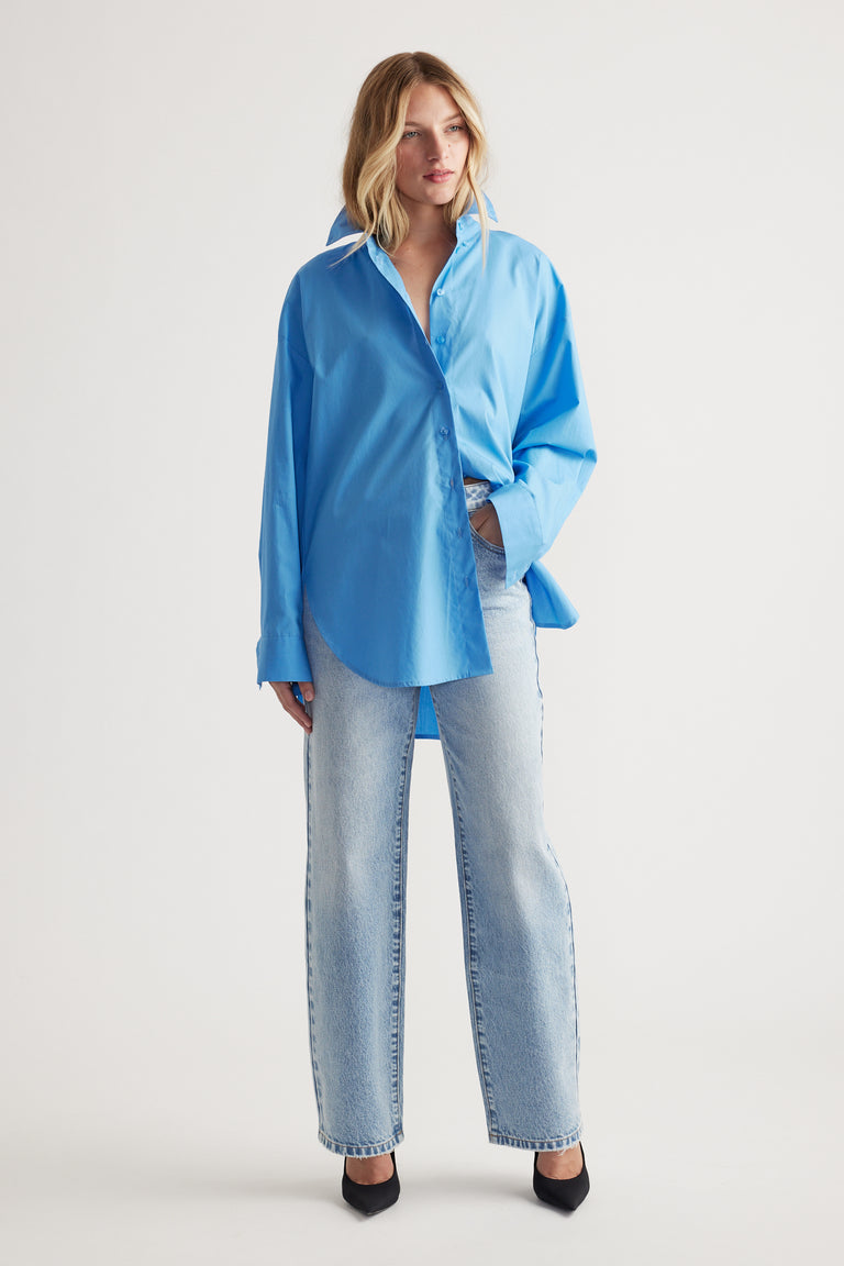 Woman wearing a relaxed fit bright blue oversized shirt paired with light wash straight-leg jeans and black heels.