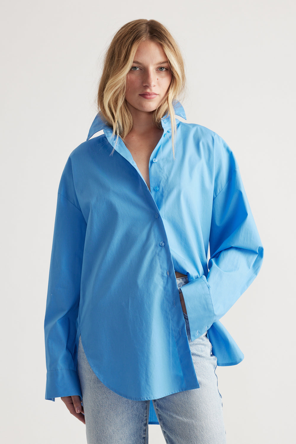 Woman wearing a relaxed oversized light blue shirt with a high collar paired with light wash denim jeans.