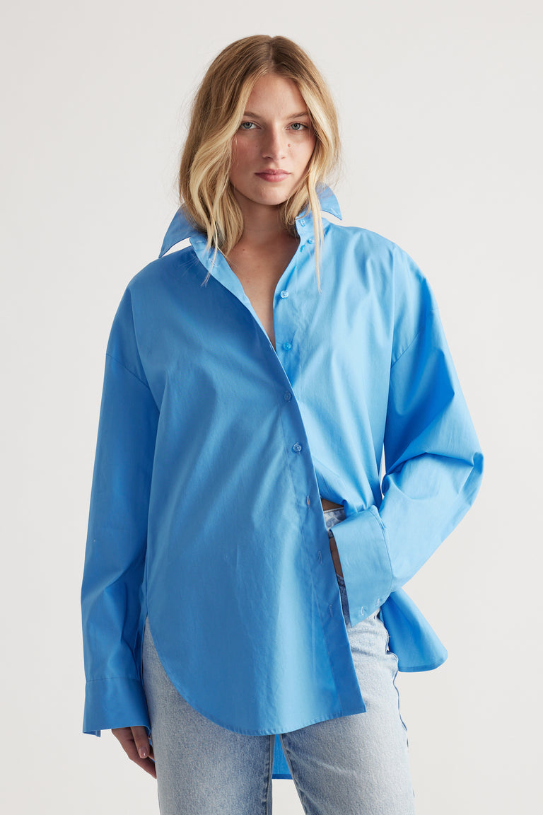 Woman wearing a relaxed oversized light blue shirt with a high collar paired with light wash denim jeans.