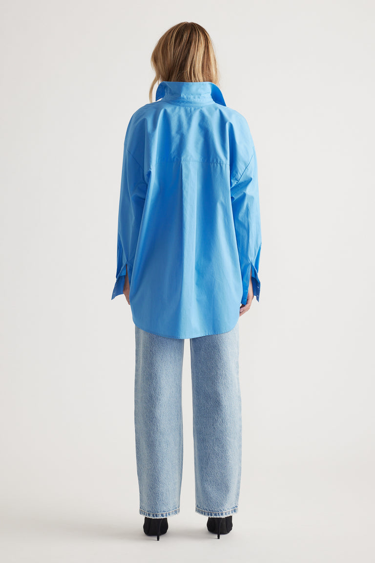 Woman wearing a relaxed fit oversized blue shirt paired with straight-leg light wash denim jeans and black heels, back view.