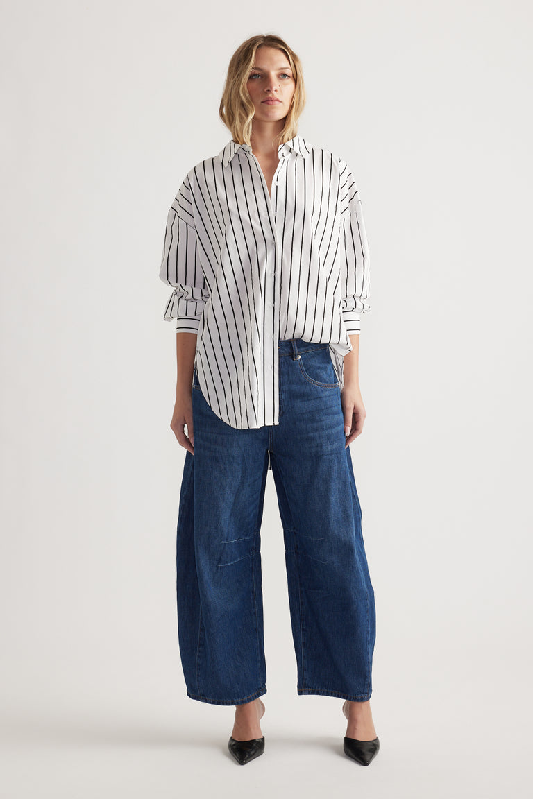 Woman wearing a relaxed fit striped shirt with rolled sleeves paired with wide-leg dark blue denim jeans and black heels
