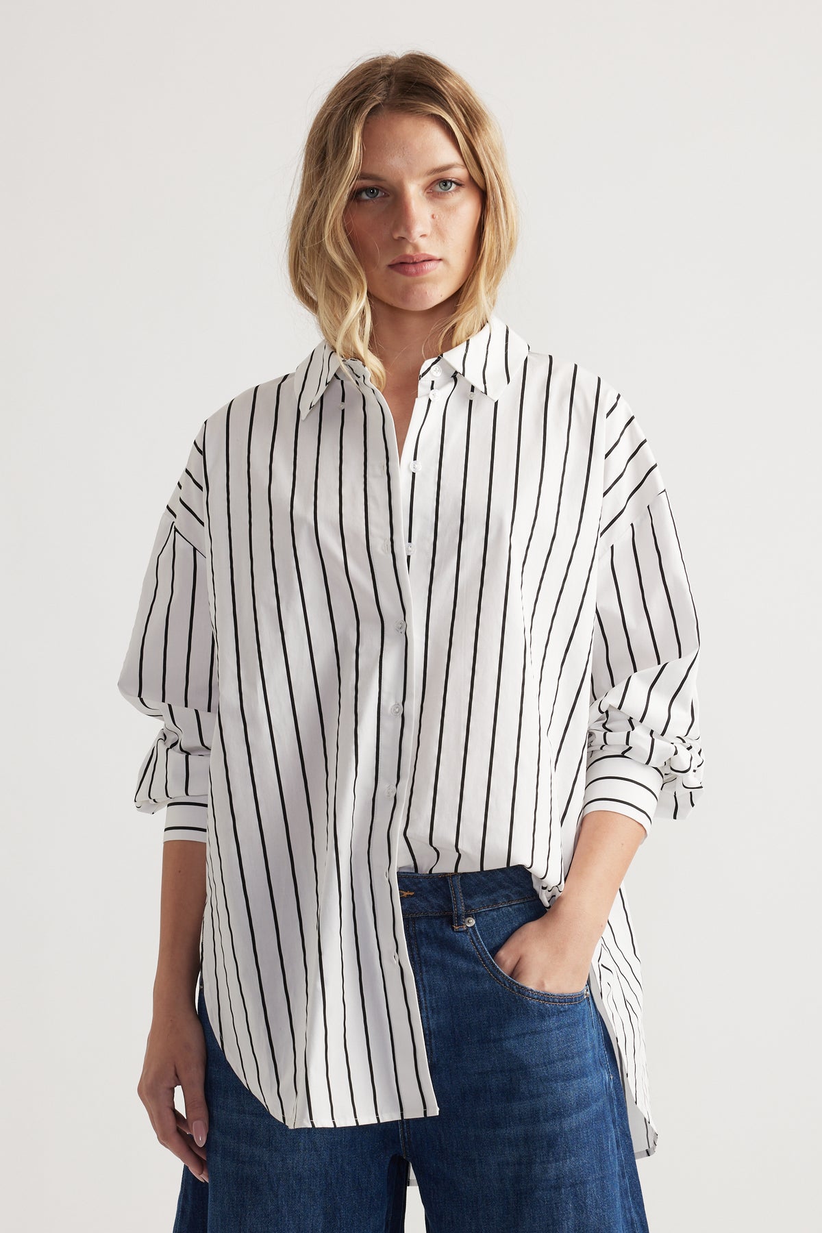 Woman wearing a white oversized shirt with black vertical stripes paired with loose dark blue denim jeans