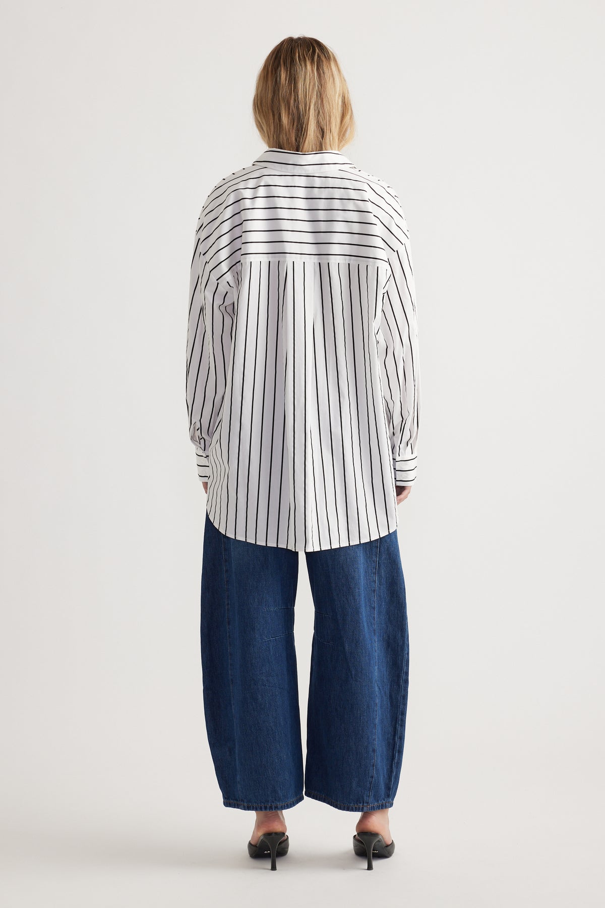 Rear view of a woman wearing a loose striped long sleeve shirt paired with wide-leg dark blue denim pants and black heels