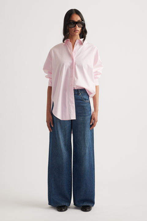 Woman wearing a light pink oversized button-up shirt paired with wide-leg dark blue denim jeans and sunglasses