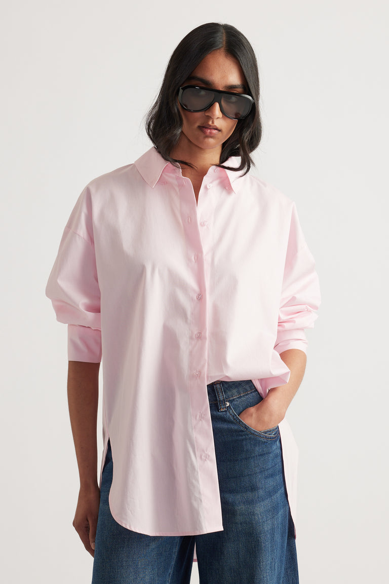 Woman wearing a light pink oversized shirt with long sleeves paired with dark blue denim jeans and black sunglasses