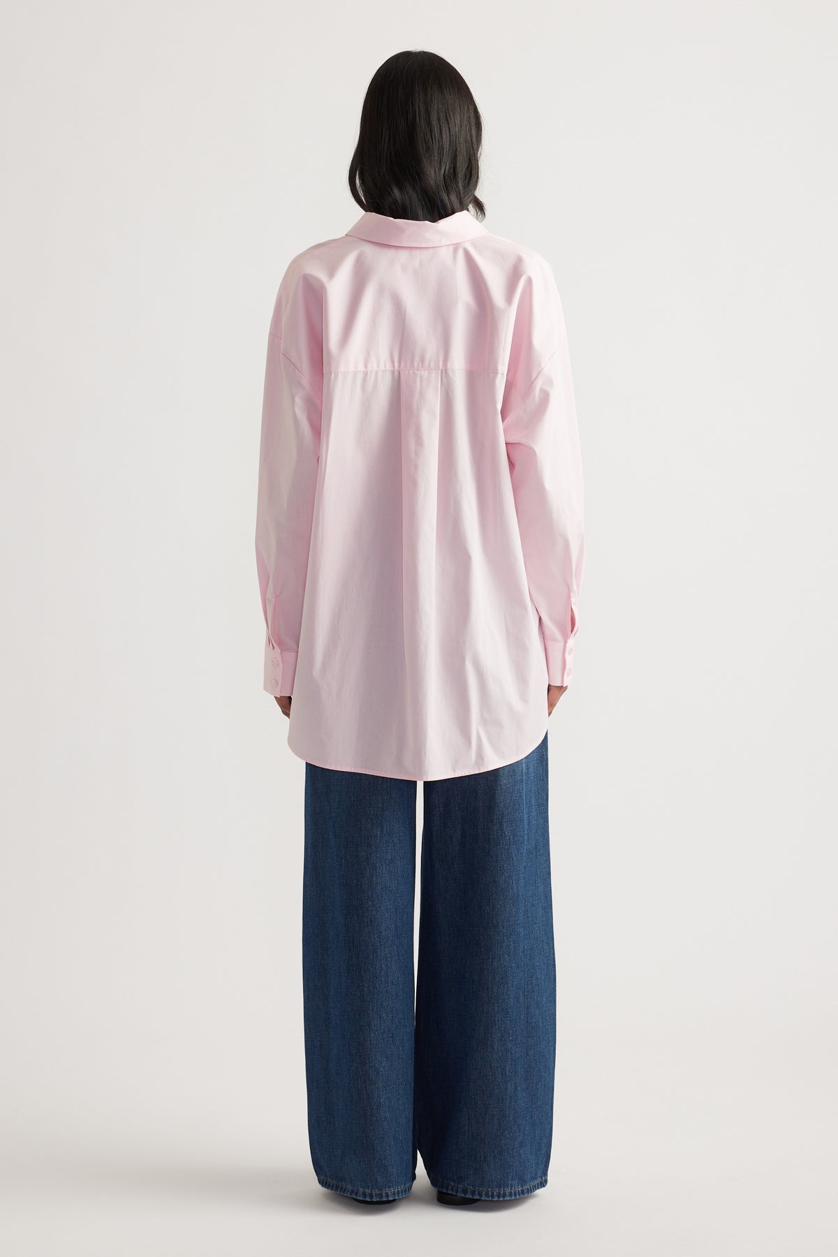 Rear view of woman wearing a light pink oversized shirt with long sleeves and wide-leg dark denim jeans