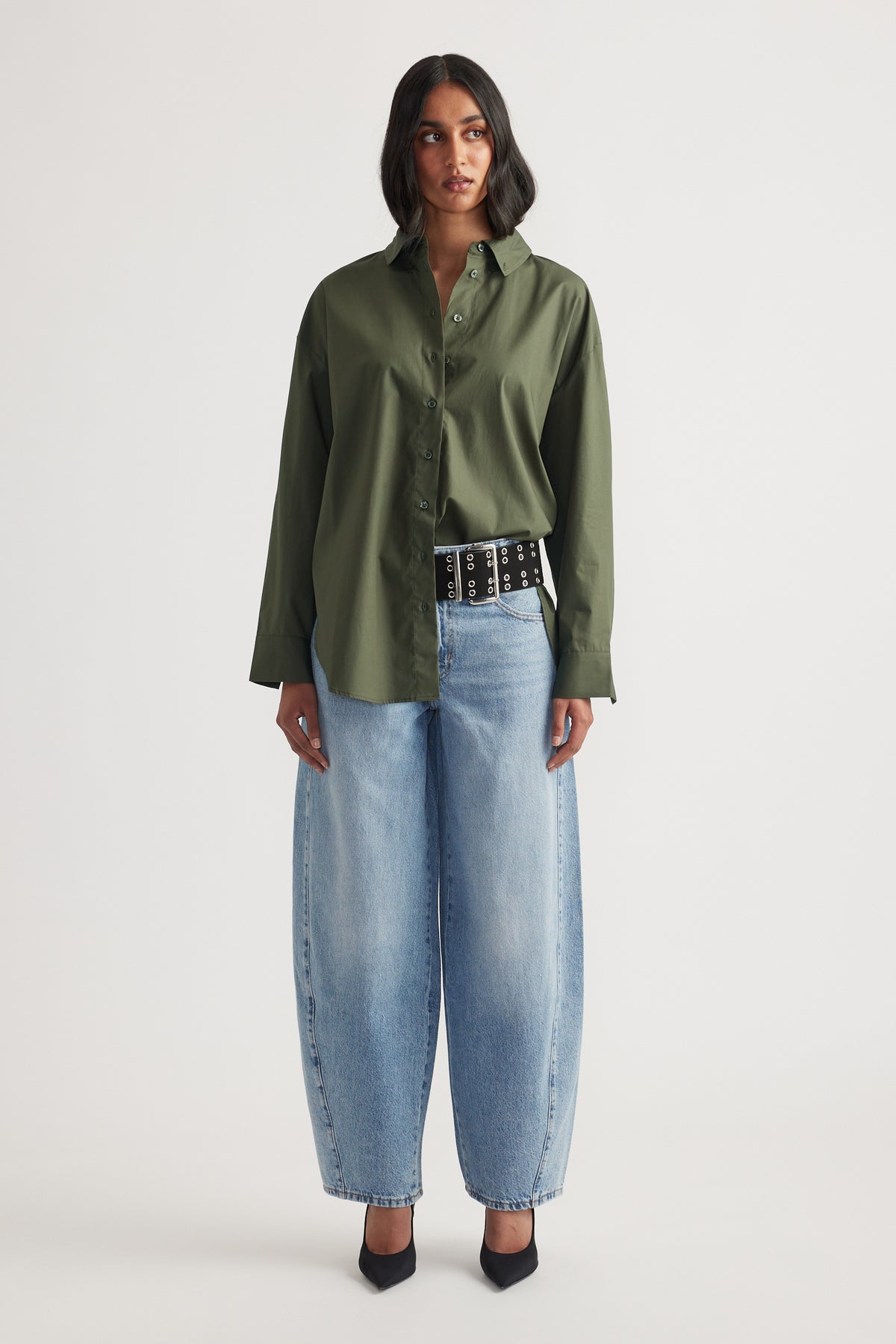Woman wearing an oversized olive green shirt paired with wide-leg light blue jeans and black pointed heels