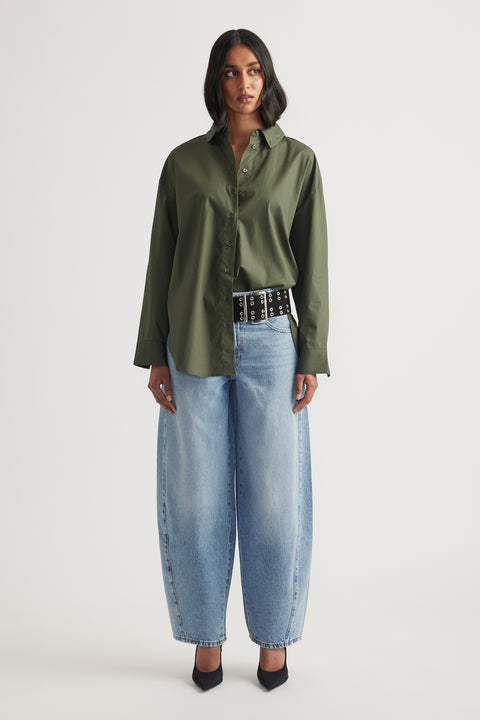 Woman wearing an oversized olive green shirt paired with wide-leg light blue jeans and black pointed heels