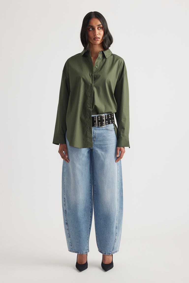 Woman wearing an oversized olive green shirt paired with wide-leg light blue jeans and black pointed heels