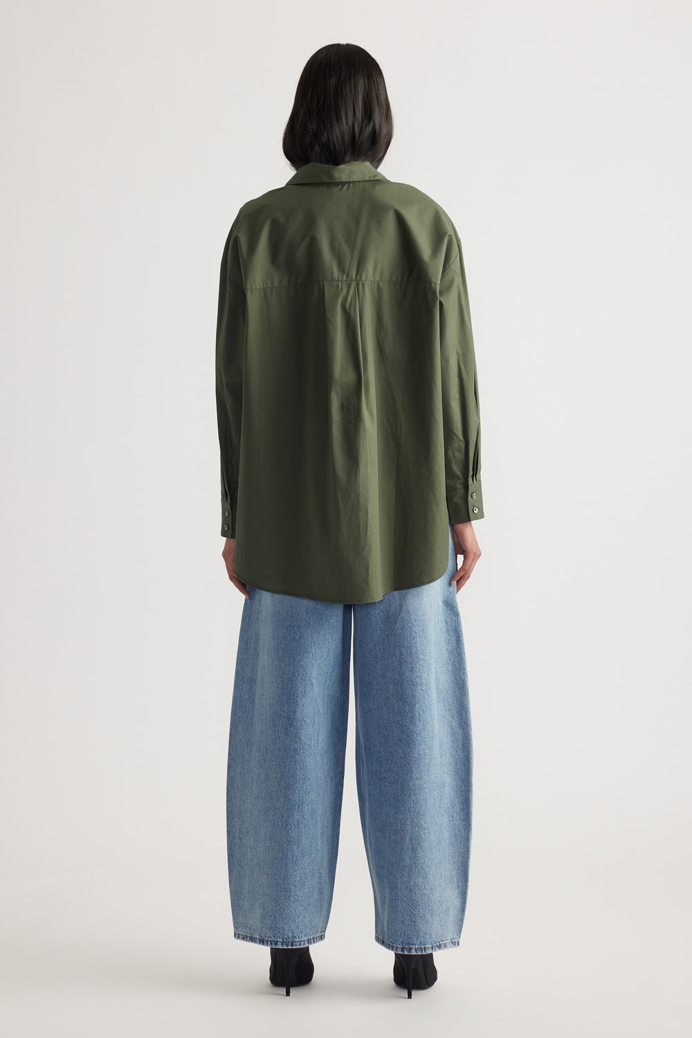 Woman seen from back wearing oversized olive green shirt with button cuffs and wide leg light blue denim jeans