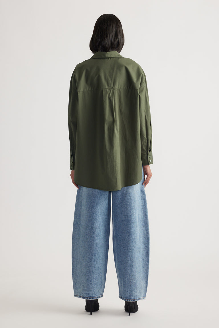 Woman seen from back wearing oversized olive green shirt with button cuffs and wide leg light blue denim jeans