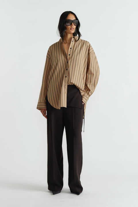 Woman wearing an oversized tan shirt with black vertical stripes paired with loose black wide-leg pants and dark sunglasses.