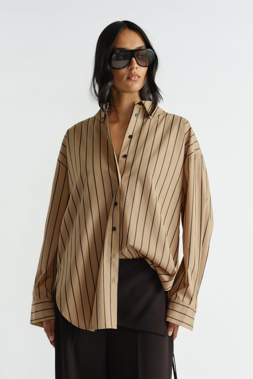 Woman wearing a relaxed fit beige striped oversized shirt paired with loose black pants and large sunglasses.