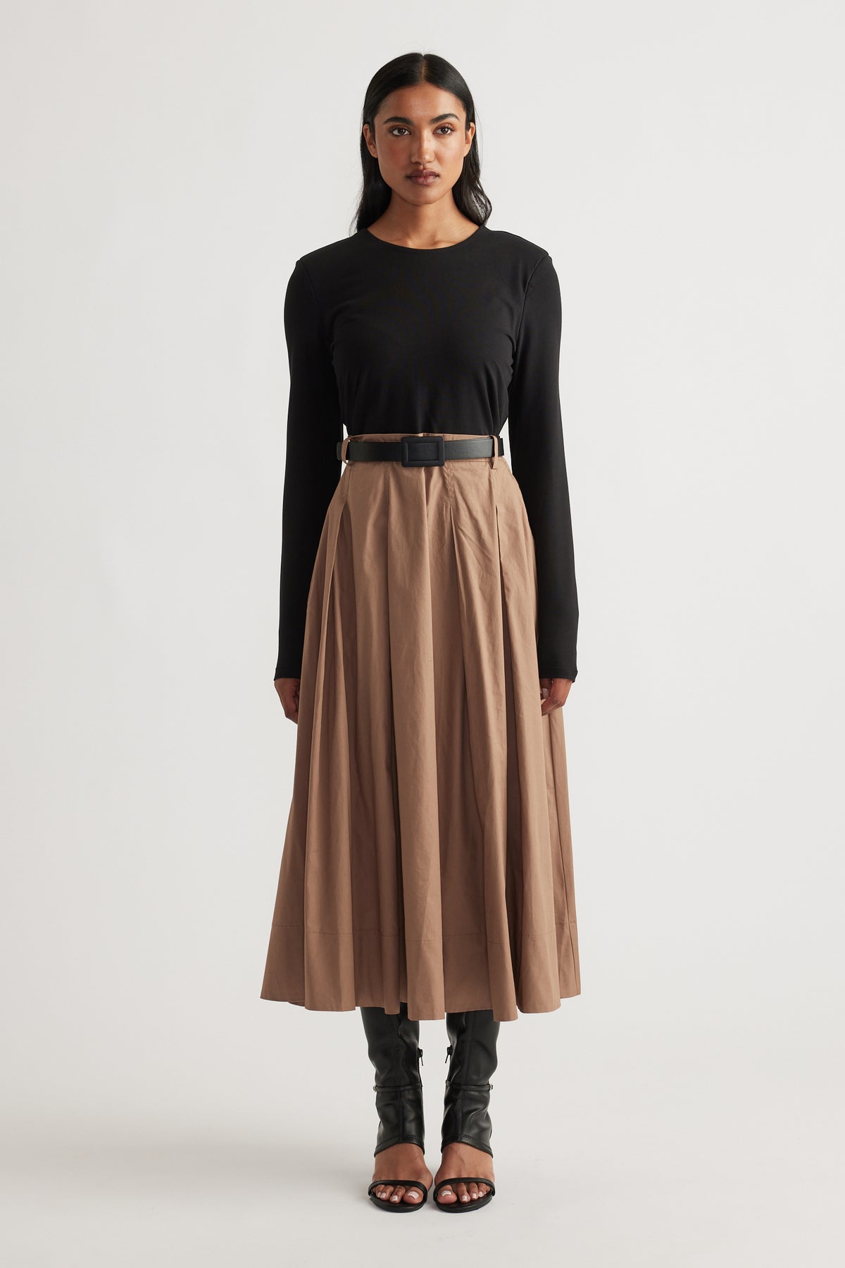 Front view of a long sleeve black top paired with a high-waisted tan midi skirt and black heeled sandals and boots layered underneath