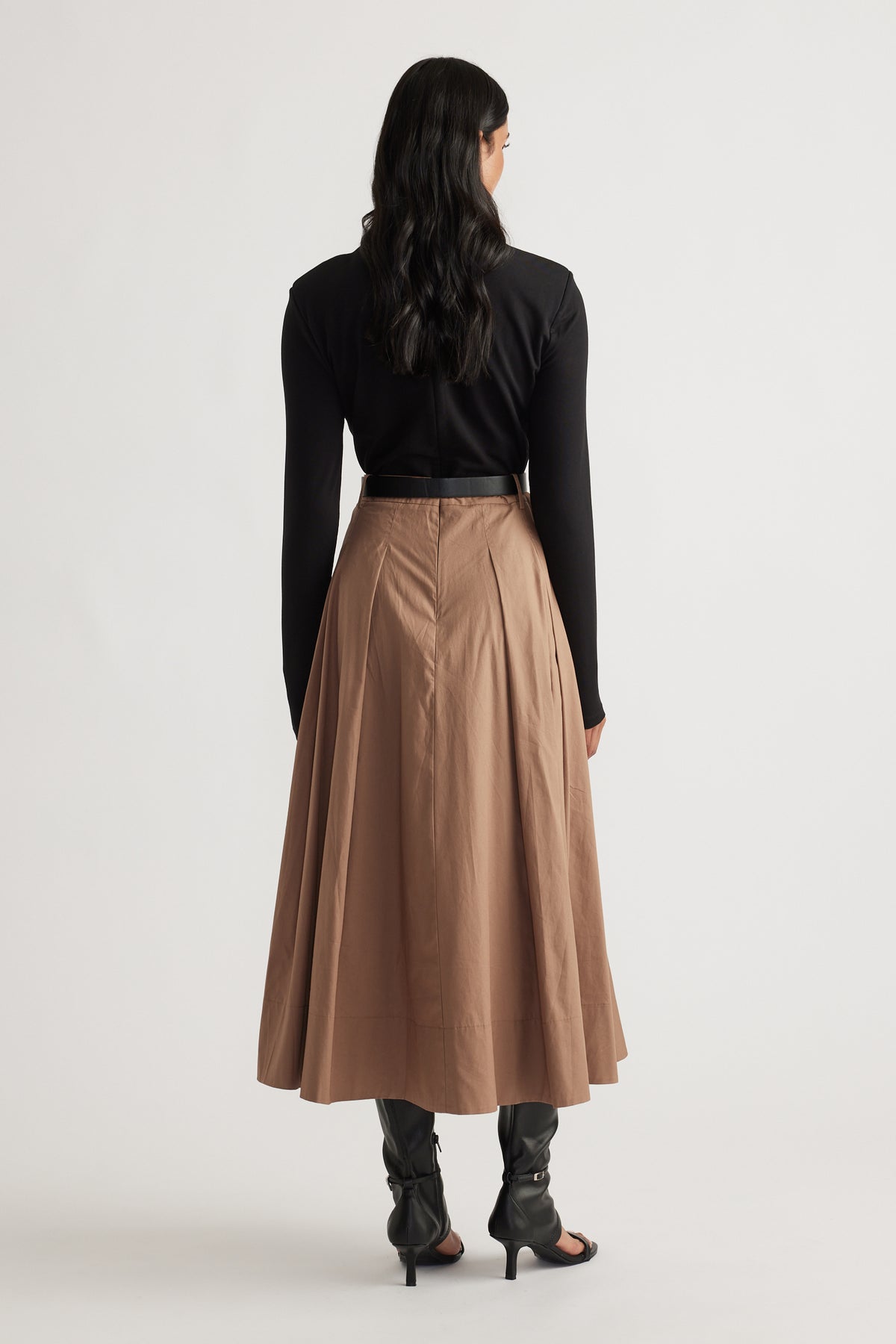 Back view of woman wearing a high-waisted brown midi skirt paired with a fitted black long sleeve top and heeled boots.