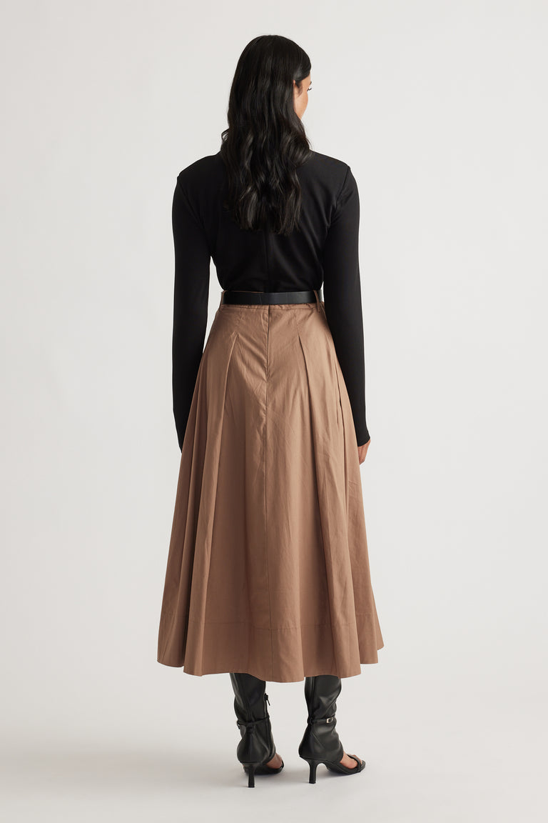 Back view of woman wearing a high-waisted brown midi skirt paired with a fitted black long sleeve top and heeled boots.