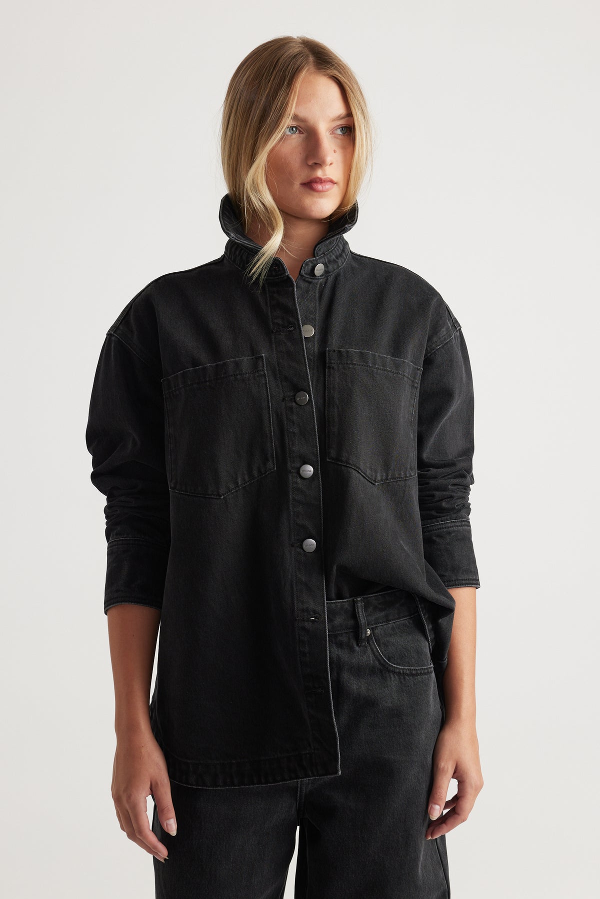 Woman wearing black denim shirt with snap buttons and chest pockets paired with black denim jeans for a modern casual look