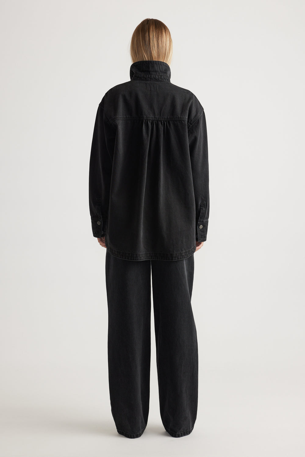 Woman seen from behind wearing an oversized black denim shirt paired with loose black wide-leg pants
