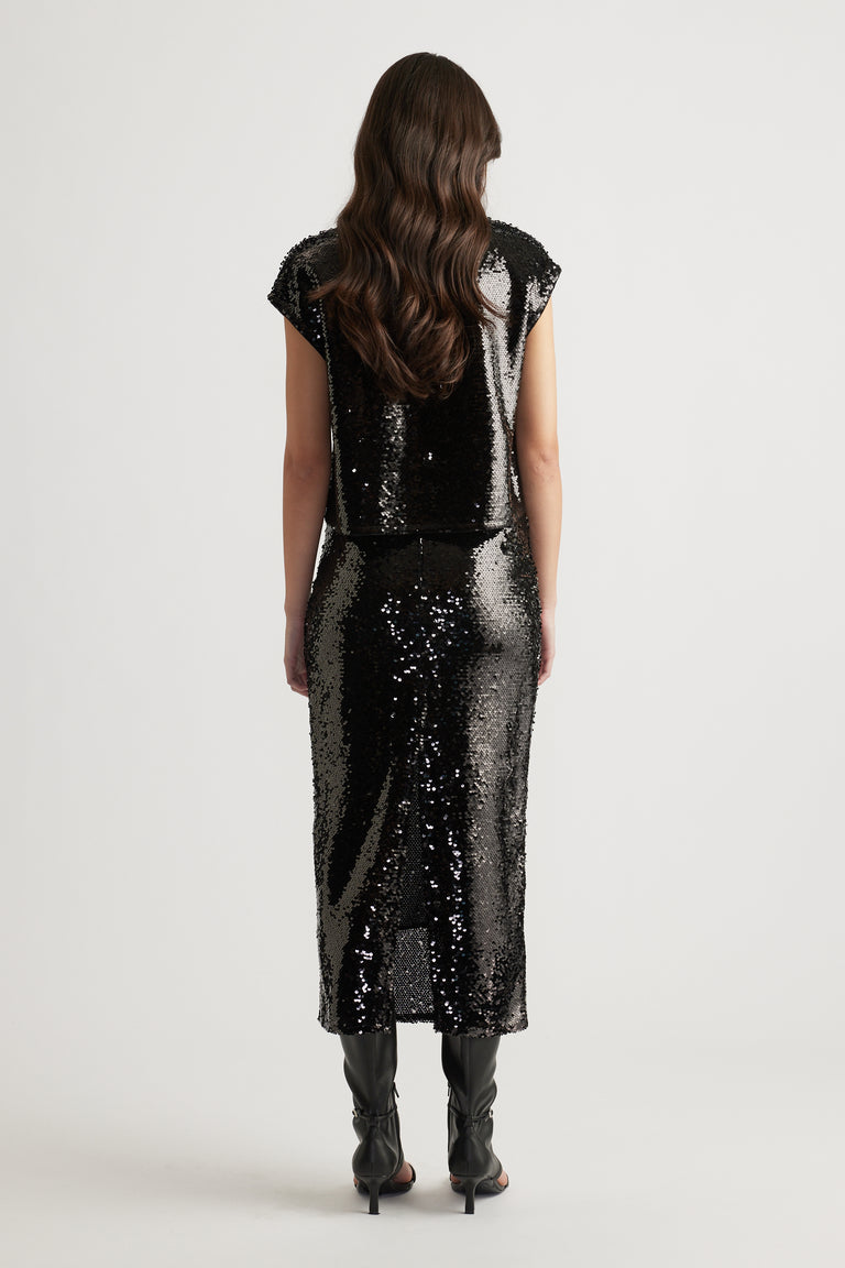 Woman wearing a black sequin shell top and matching midi skirt paired with black heeled boots for a polished look