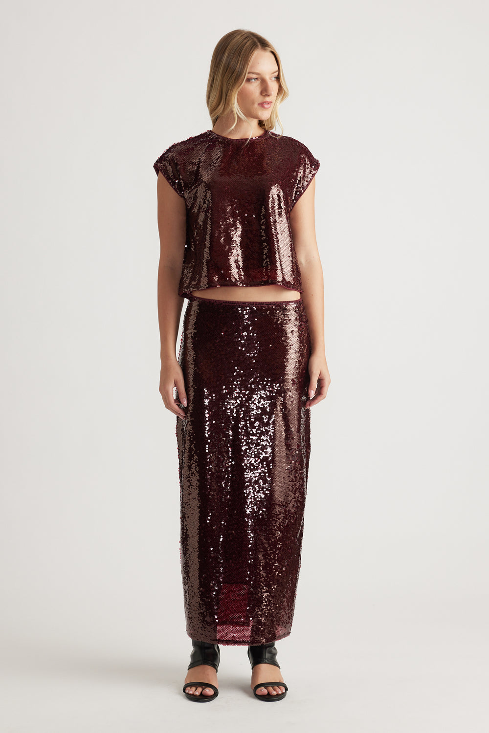Woman wearing a plum sequin shell top and matching high-waisted sequin skirt paired with black open-toe sandals