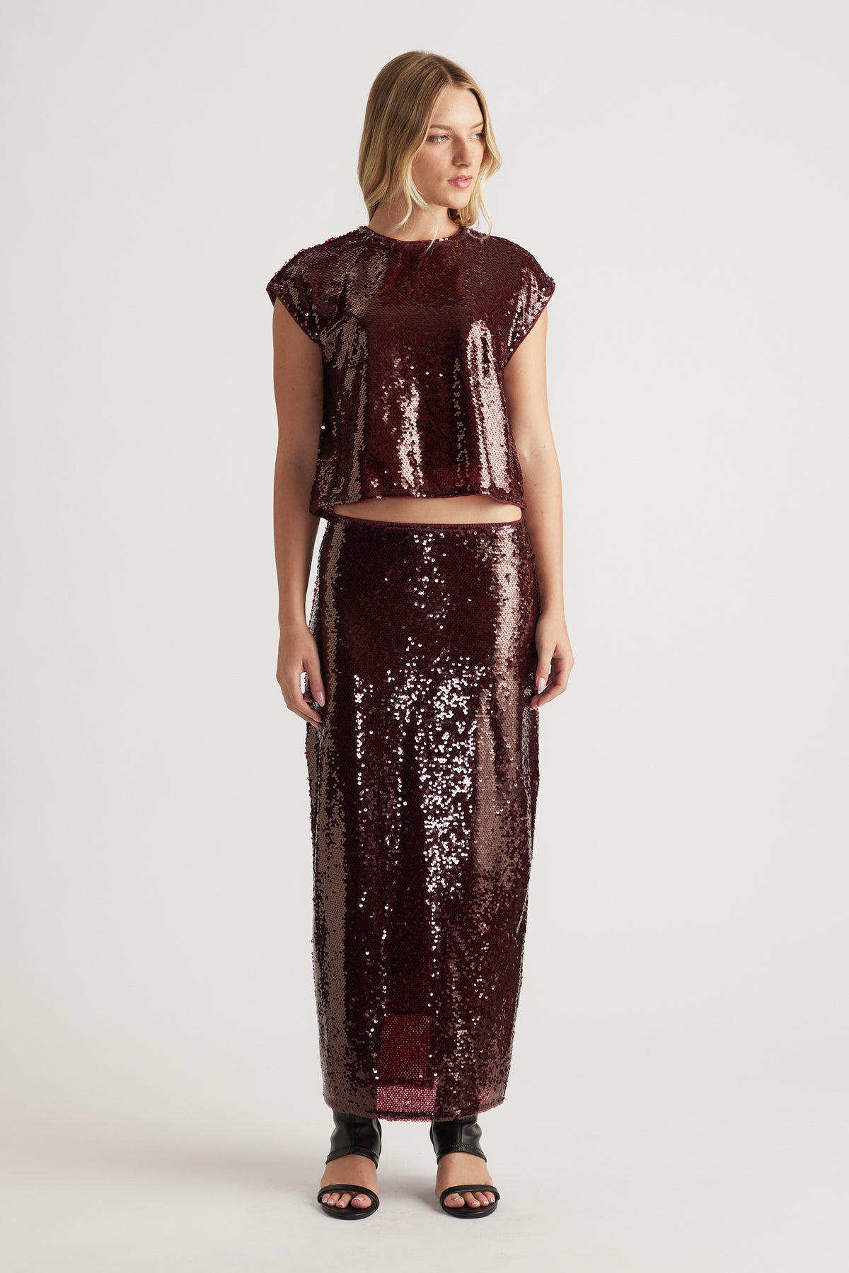 Woman wearing a plum sequin shell top and matching high-waisted sequin skirt paired with black open-toe sandals