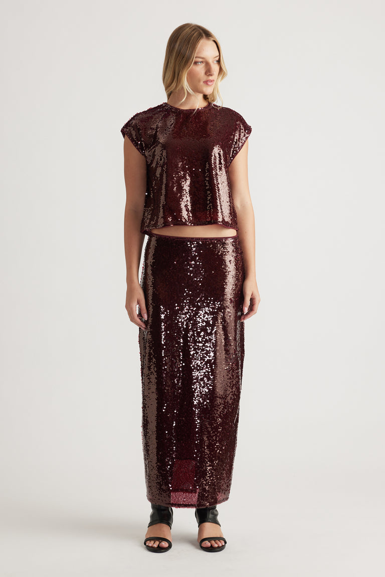 Woman wearing a plum sequin shell top and matching high-waisted sequin skirt paired with black open-toe sandals