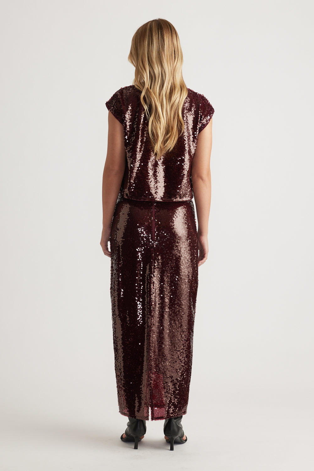 Woman wearing a plum sequin shell top and matching skirt with a sleek, shimmering texture and relaxed silhouette viewed from behind