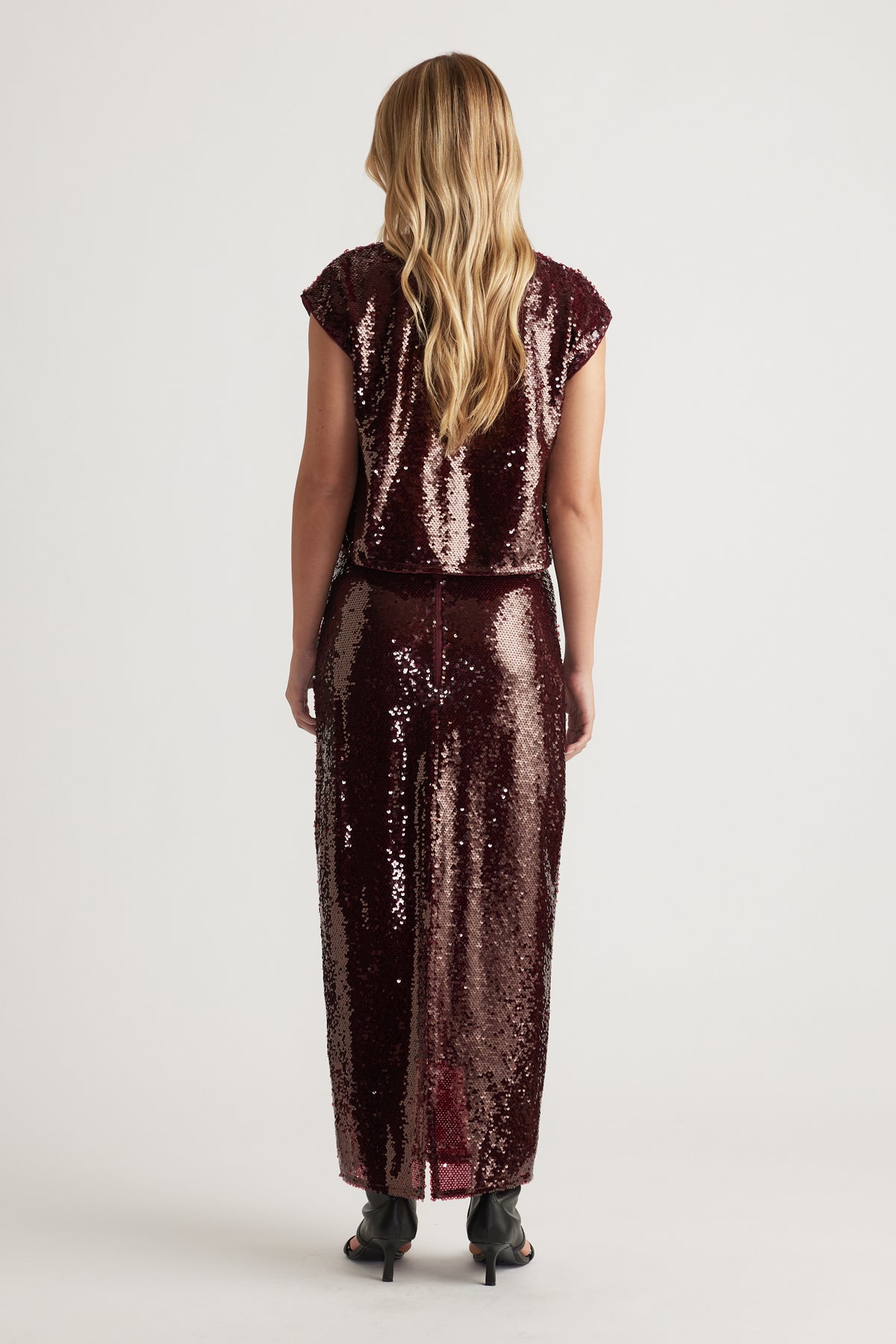 Woman wearing a plum sequin shell top and matching skirt with a sleek, shimmering texture and relaxed silhouette viewed from behind