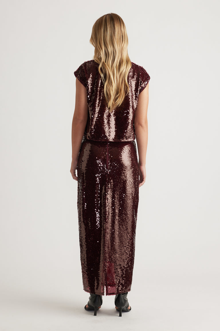 Woman wearing a plum sequin shell top and matching skirt with a sleek, shimmering texture and relaxed silhouette viewed from behind