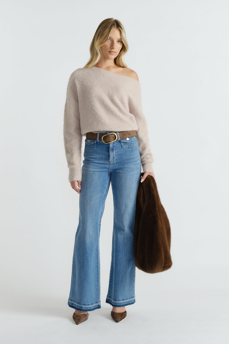 Woman wearing a soft beige off-shoulder knit sweater tucked into high-waisted flared blue jeans with brown accessories