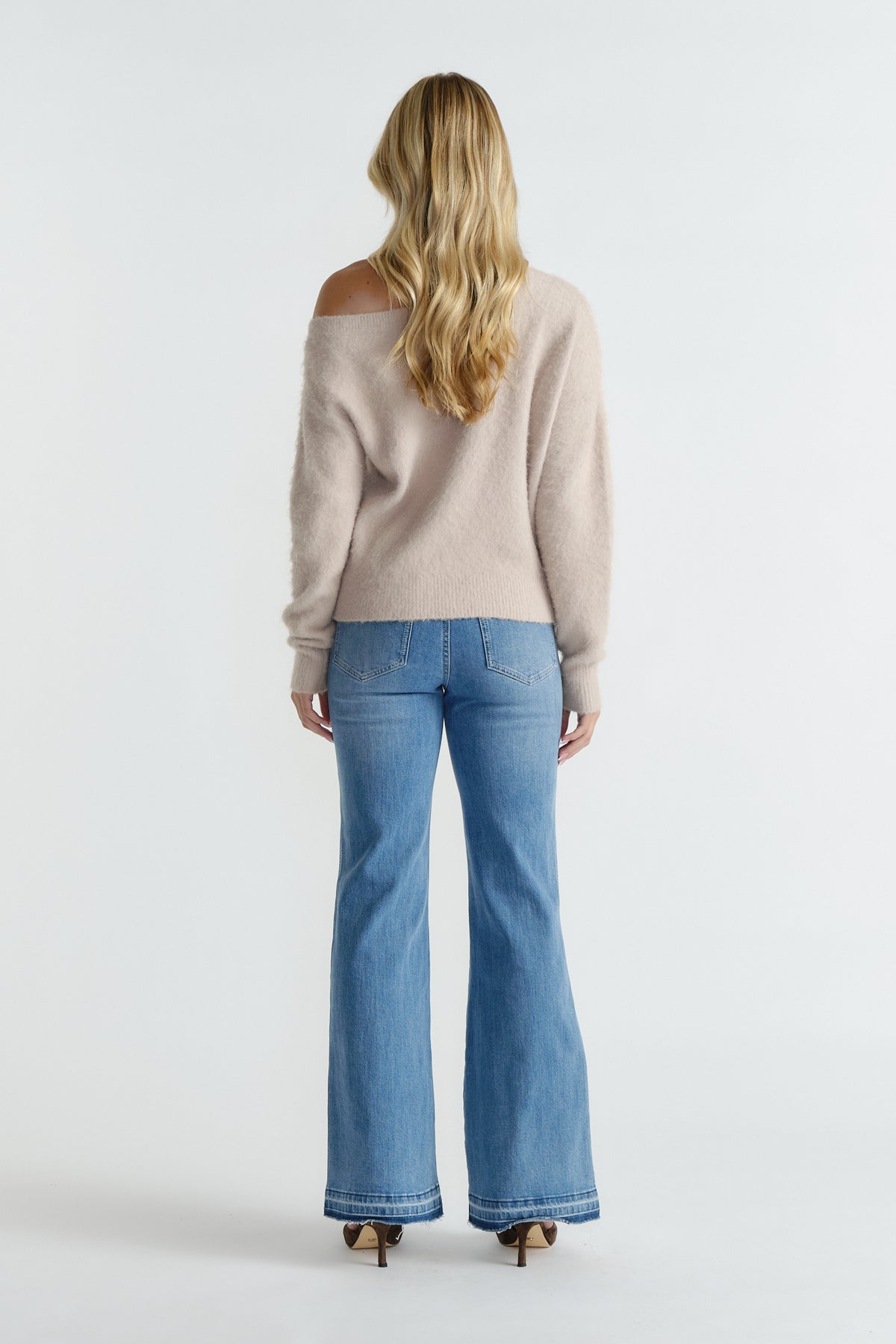 Rear view of woman wearing a soft beige off-shoulder knit paired with light-wash flared jeans and heels