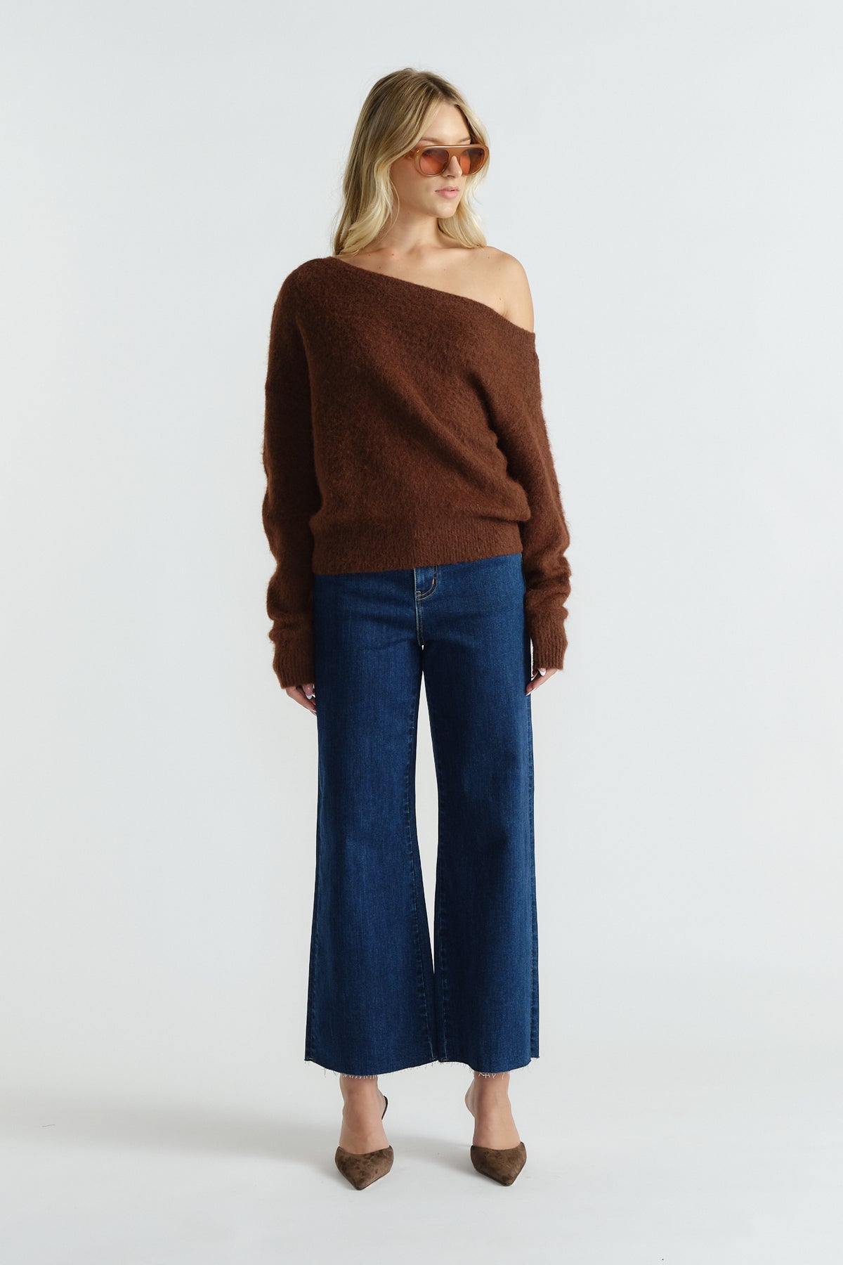 Woman wearing a soft brown off-shoulder knit sweater paired with wide-leg dark blue jeans and pointed shoes