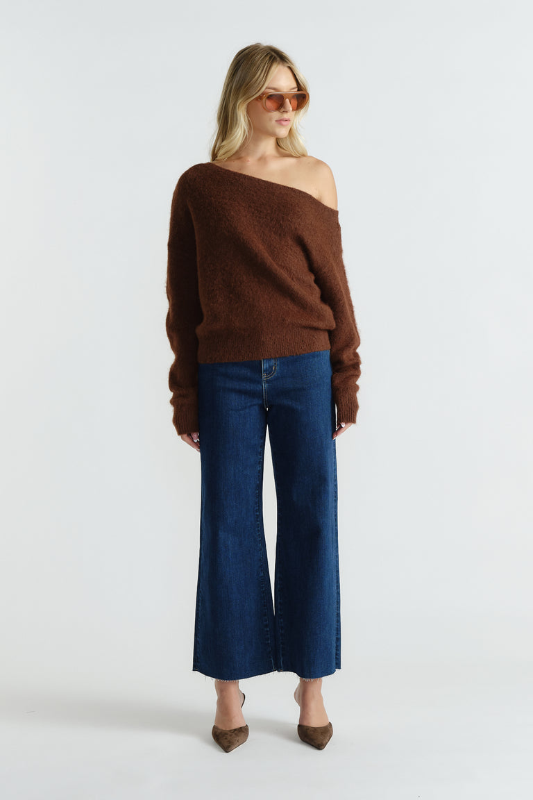 Woman wearing a soft brown off-shoulder knit sweater paired with wide-leg dark blue jeans and pointed shoes