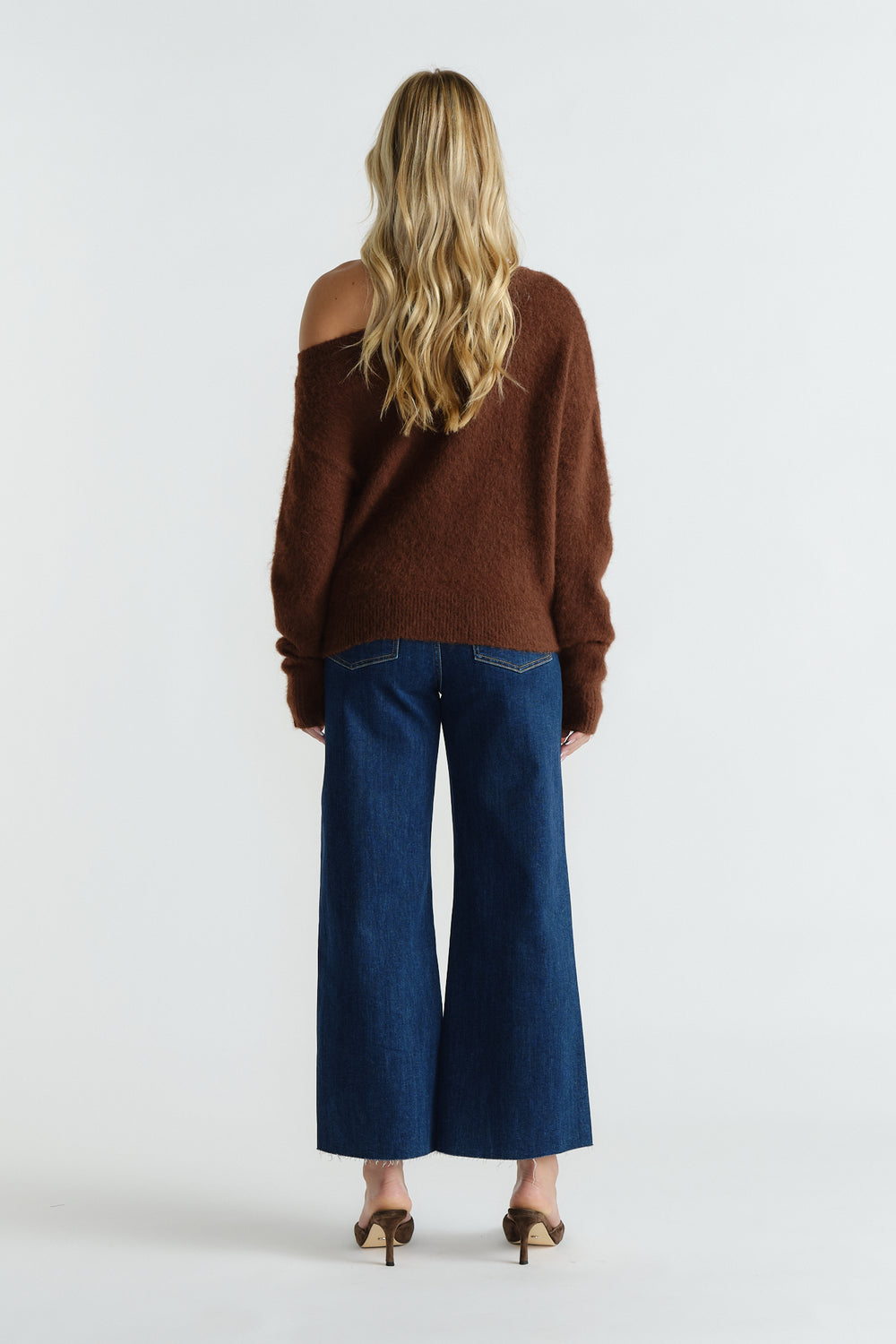 Woman wearing a chocolate brown off-shoulder knit paired with high-waisted wide-leg dark blue jeans and heels