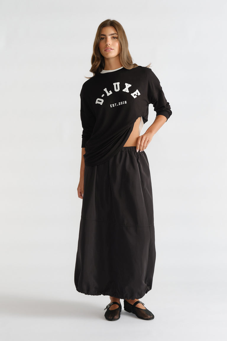 Woman wearing a black long sleeve logo top paired with a loose black maxi skirt and black ballet flats