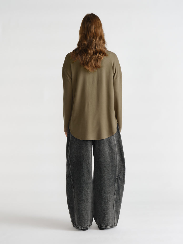 Woman shown from behind wearing a loose olive long sleeve top paired with wide-leg black faded denim jeans