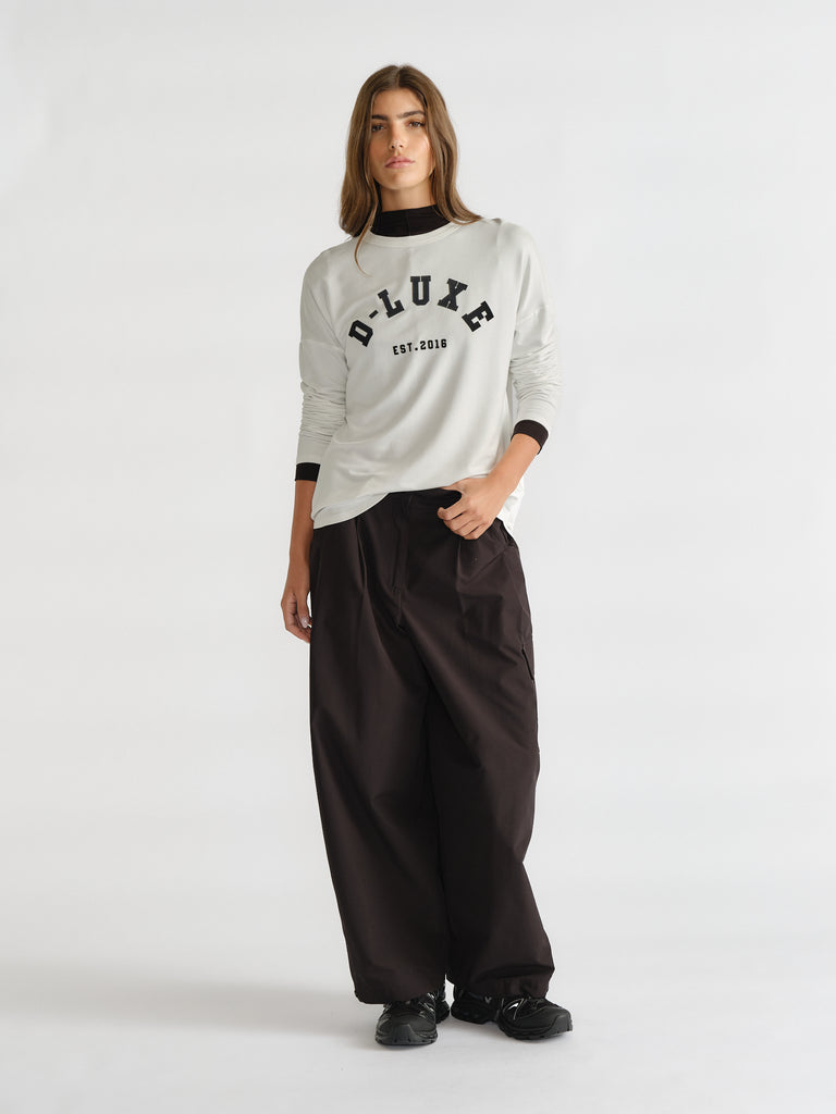 Woman wearing an ivory long sleeve top with logo detail paired with loose black wide-leg pants and black shoes