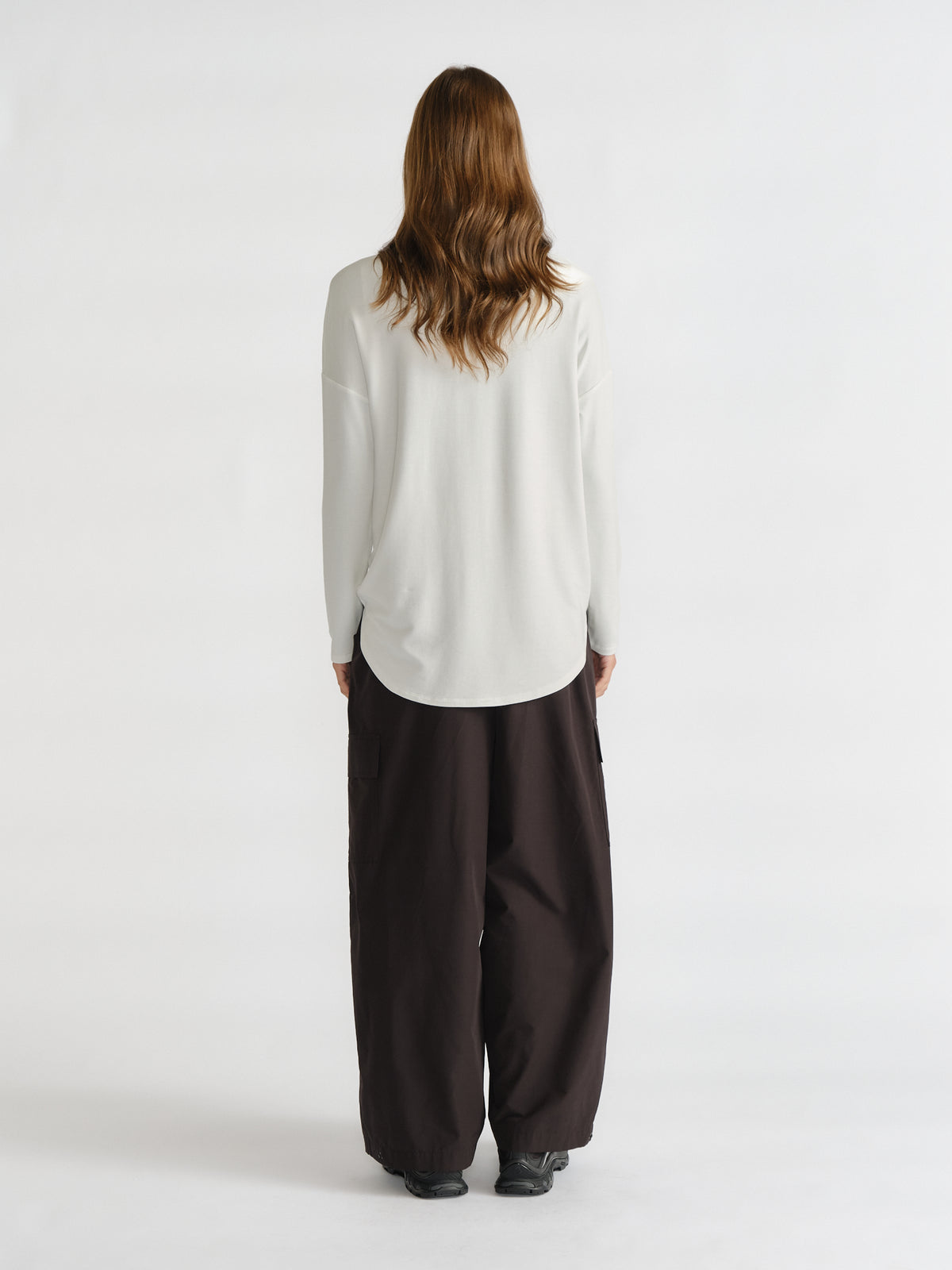 Woman shown from behind wearing a relaxed fit ivory long sleeve top with curved hem paired with loose black pants and black shoes